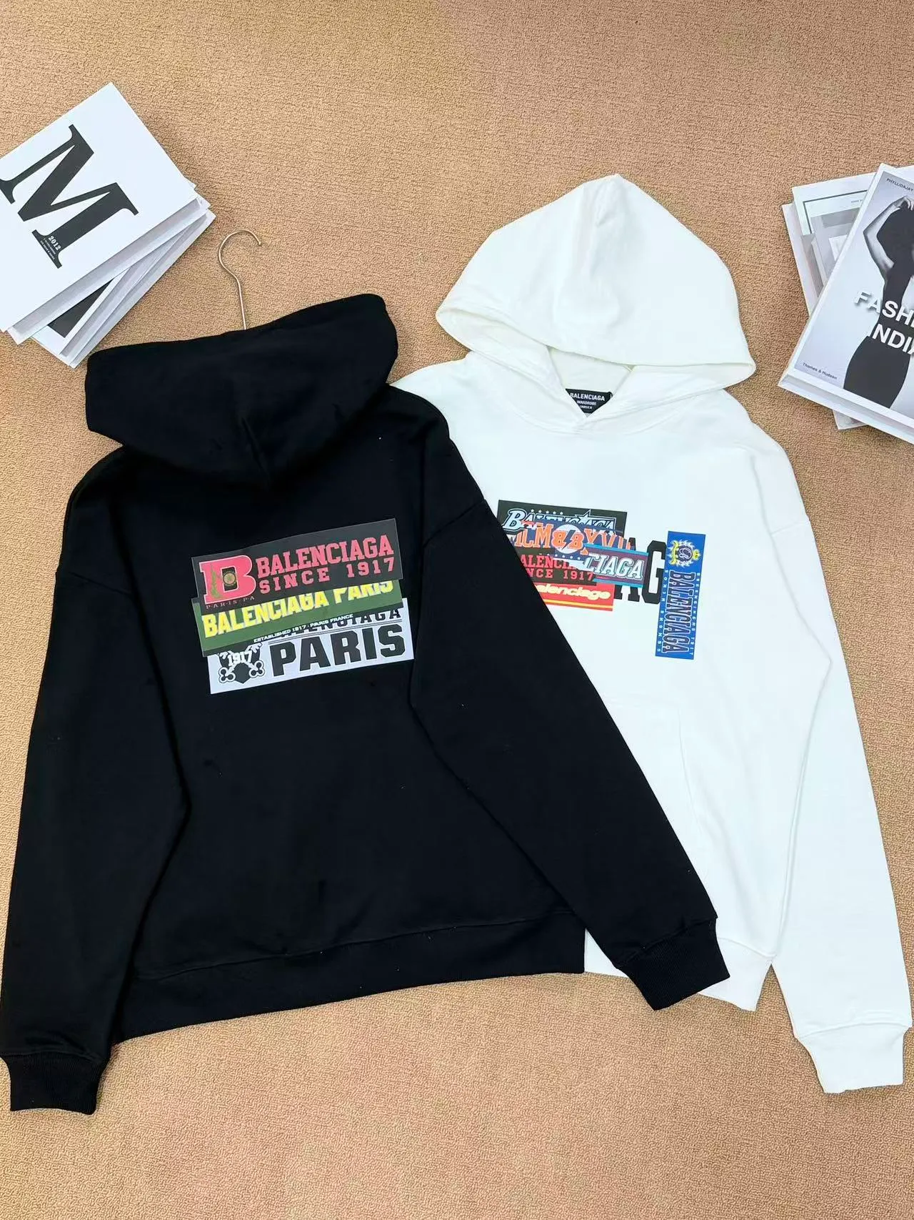 Style No. 2202 • Color: Black / White available • Version: Loose shoulder oversize version, regardless of figure, same style for men and women • Style: Pullover hooded sweatshirt, front kangaroo pocket, casual Versatile 🧶Fabric technology: Made of 420 high-gram weight cotton terry fabric, soft and thick to the touch, comfortable and Breathable on the upper body; threaded cuffs + hem, not easy to deform after long-term wear. The printing adopts high-definition offset printing, multi-layer label sticker style pattern, the color is full and firm, and the large pattern on the back has strong visual impact. 🎨Design highlights: Retro collage label printing, multi-layer BALENCIAGA letter logo superimposed, full of street fashion sense. Simple hooded basic version + exaggerated back print, low-key and recognizable, with a high-end and lazy atmosphere. 🧥Wearing scenarios: Suitable for daily commuting, shopping and outings, and campus wear. The lower body can be worn with jeans, sports pants, or shark pants. The loose fit hides the flesh and makes you look slimmer. It is perfect for couples. Sizes m l xl
